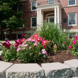 A colorful flower garden in front of a brick building entrance.
