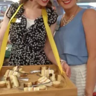 Two women holding a tray with assorted cheeses at an event.