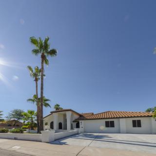 A single-story house with a tiled roof, surrounded by palm trees, under a clear blue sky.