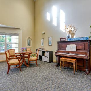 A cozy living room with a piano, table, and chairs near a large window.