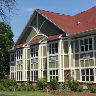 A residential building with large windows and a red roof surrounded by trees.