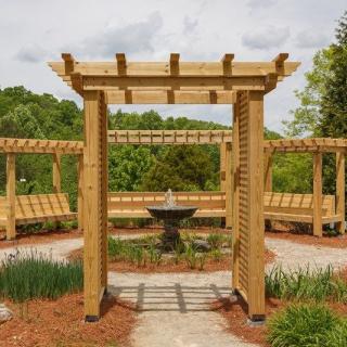 A beautiful garden featuring a wooden pergola and a central fountain.