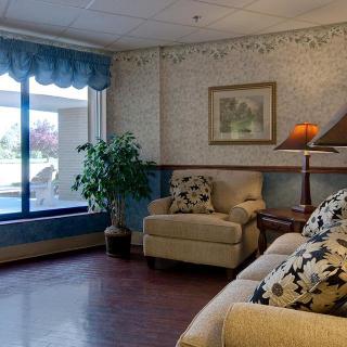 A cozy living room with a sofa, armchair, lamp, and large window overlooking an outdoor area.