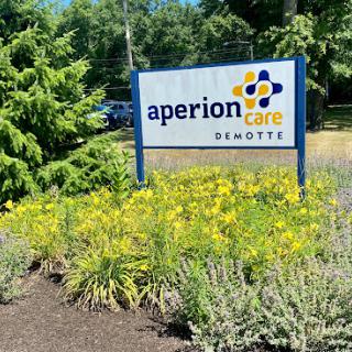 Signage for Aperion Care, surrounded by blooming flowers and greenery.