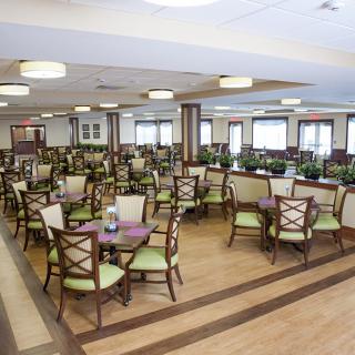 A spacious dining area with neatly arranged tables and chairs, featuring wood flooring and ample lighting.