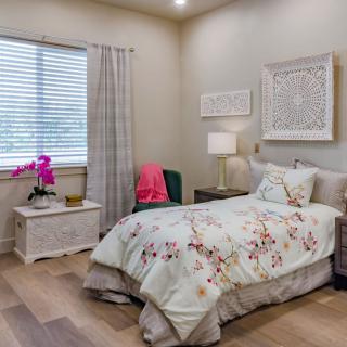 A cozy bedroom with a single bed featuring floral bedding, complemented by a nightstand and decorative wall art.