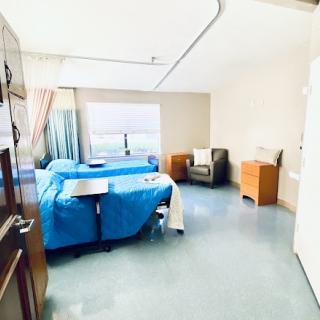 A spacious and well-lit hospital patient room featuring blue bedding and comfortable seating.