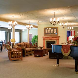 A spacious lobby featuring comfortable seating, a grand piano, chandeliers, and a fireplace with an American flag displayed on the wall.