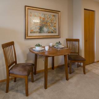 A cozy dining area with a wooden table set for two, accompanied by matching chairs and adorned with wall art.