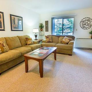 A cozy living room with comfortable sofas and a coffee table, decorated with artwork and a large window providing natural light.