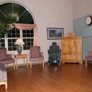 A cozy living room featuring a variety of seating options including chairs and a couch, with a large window and decorative elements such as a lamp, clock, and indoor plant.