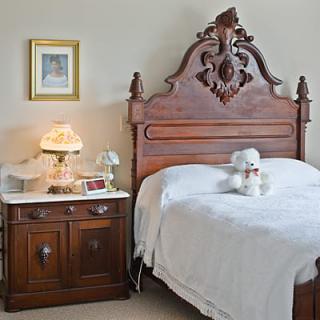 A vintage bedroom featuring an antique wooden headboard and a classic nightstand with a decorative lamp.
