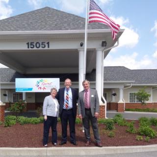 A group of three people standing in front of a building with an American flag.
