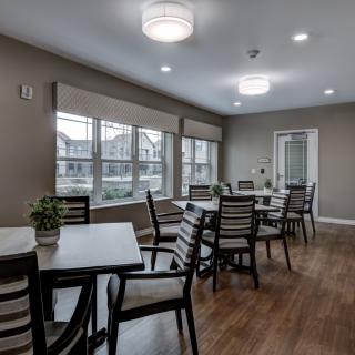 A neatly arranged dining area with multiple tables and chairs, complemented by large windows and modern lighting fixtures.