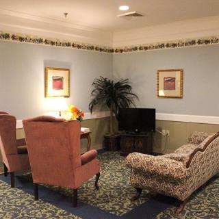 A cozy living room with comfortable chairs, a couch, and a TV, adorned with artwork and a potted plant.