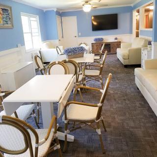 A bright lounge area with tables, chairs, sofas, and a television.