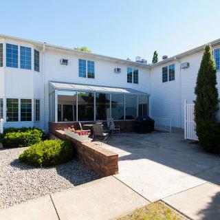 A spacious backyard patio area of a two-story house with large windows and greenery.