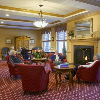 A cozy lounge area with seniors seated around a fireplace.