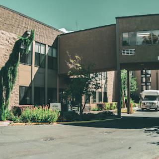 A view of a modern building with greenery and a vehicle in the foreground.