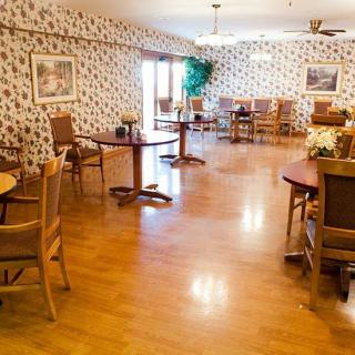 A cozy dining area with wooden floors, tables, and chairs, accented by floral wallpaper and decorative plants.