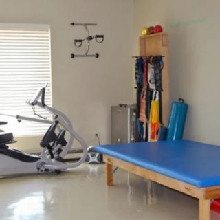 A well-equipped physical therapy room with a stationary bike, treatment table, and exercise bands.