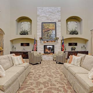 A spacious living room with a central fireplace, surrounded by sofas and armchairs, decorated with artwork and American flags.