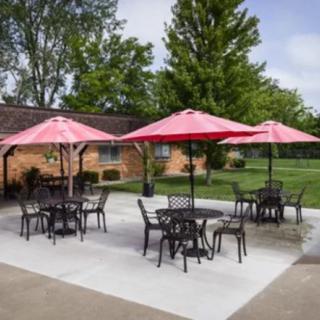 Outdoor patio area with tables, chairs, and red umbrellas surrounded by a green lawn.