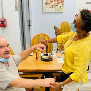 A healthcare worker assists an elderly man at a care facility, both wearing masks.