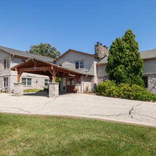 A spacious residential home with a stone exterior and a covered driveway, surrounded by lush greenery.