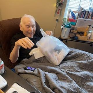 An elderly man sits in bed, smiling while reading a document.