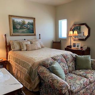 A cozy bedroom with a bed, floral sofa, decorative lamp, and artwork on the wall.