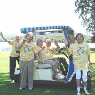 A group of people enjoying a day outdoors, gathered around a golf cart and waving.
