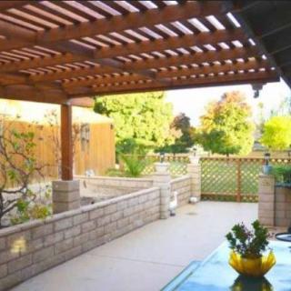 A sunny backyard patio with a wooden pergola and lush garden.