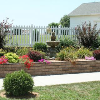 A beautifully landscaped garden featuring vibrant flowers, a decorative fountain, and a white picket fence.