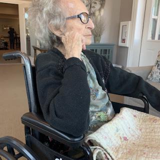 An elderly individual sitting in a wheelchair, deep in thought.