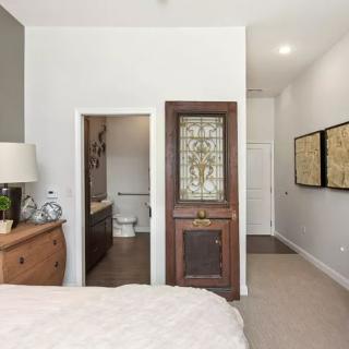 A modern bedroom featuring a cozy bed, wooden dresser, and an elegant lamp, with a glimpse into an adjoining bathroom.