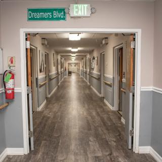 A view down a quiet hallway in a medical facility, featuring an exit sign and fire extinguisher.