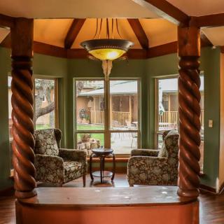 A cozy seating area with patterned chairs and a table, framed by wooden pillars and large windows.