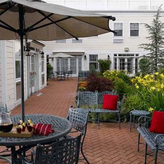 A charming patio area with outdoor furniture, umbrellas, and vibrant flowers lining a brick pathway.