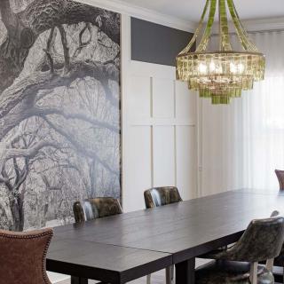 A modern dining room featuring a large table, artistic wall design, and an elegant chandelier.