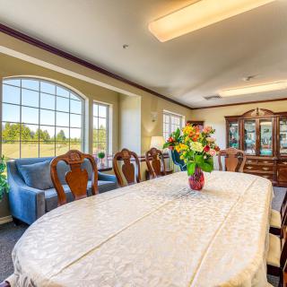 A spacious and elegant dining room with a large table, adorned with a floral centerpiece, surrounded by classic wooden chairs.
