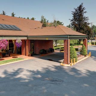 A building entrance with hanging flower baskets and a driveway surrounded by trees.