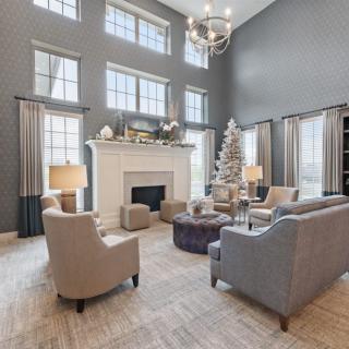 A spacious and elegant living room featuring high ceilings, large windows, and a beautifully decorated Christmas tree beside a white fireplace. The modern furniture and neutral color palette create a warm and inviting atmosphere.