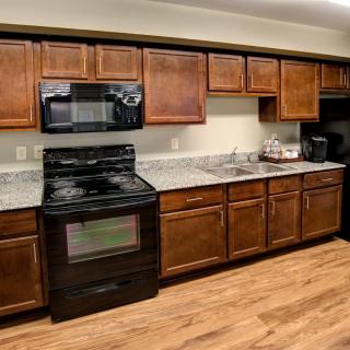A modern kitchen with wooden cabinets, black appliances, and wood flooring.