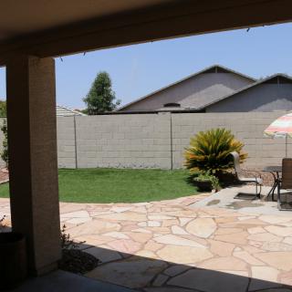 A sunny backyard with a patio area, featuring outdoor furniture and an umbrella.