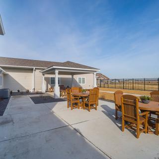A spacious backyard patio with wooden tables and chairs under a clear blue sky.