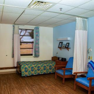 A quiet hospital room featuring a bed, two chairs, and blue walls.