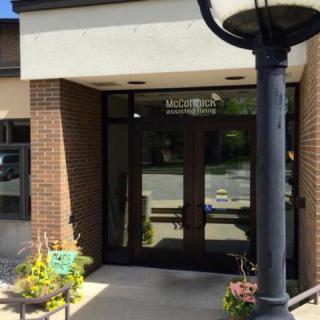 The entrance of a building with glass doors and a brick exterior, featuring potted plants and a lamppost.