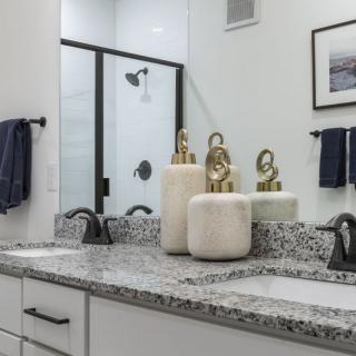 A modern bathroom with a granite countertop, double sinks, and decorative jars.