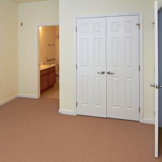 An empty bedroom featuring a double-door closet with beige carpeting.